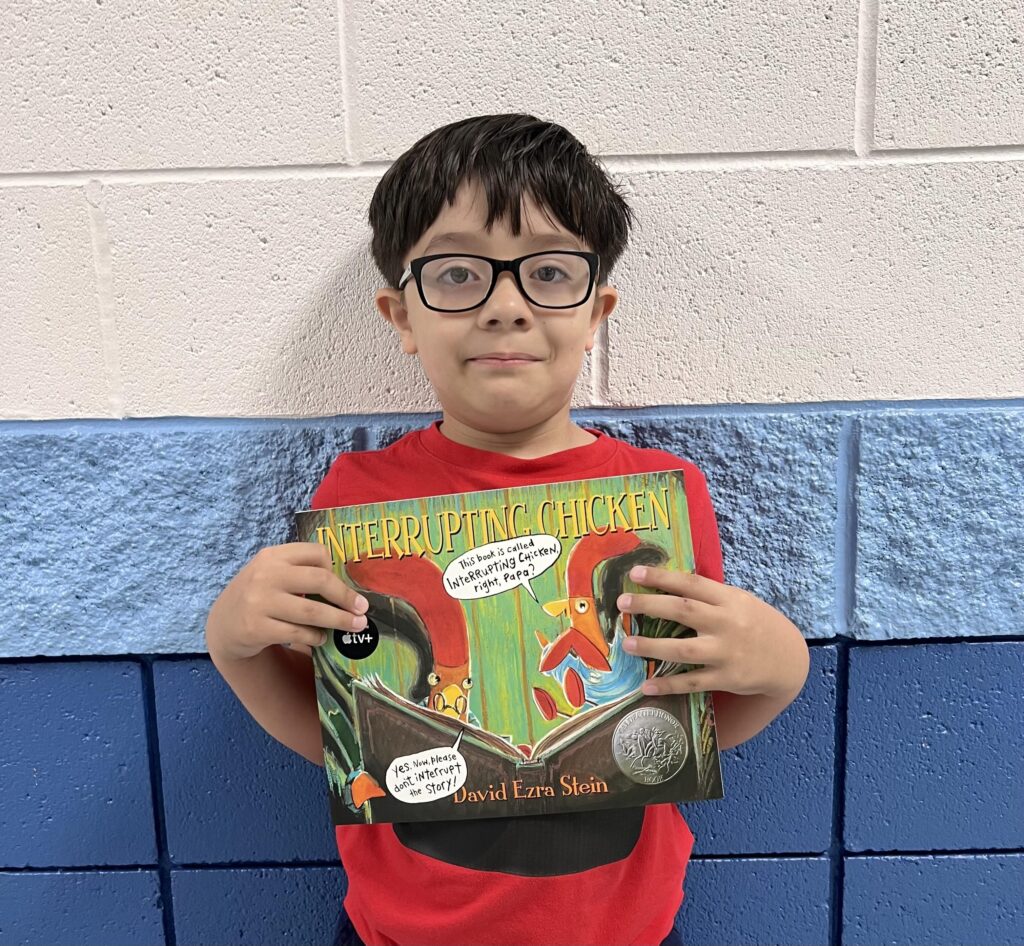 Elementary student wearing glasses holds a book he earned through a praise award.