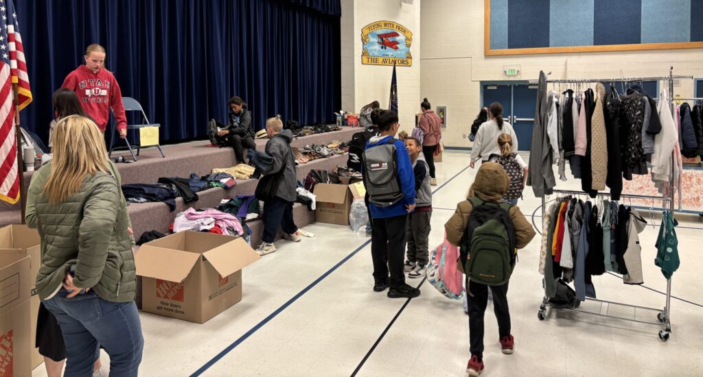 people finding gathering clothing items they need from tables set up in the gym