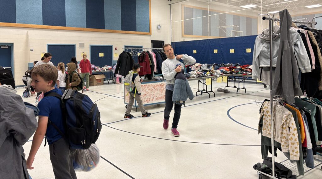 people finding gathering clothing items they need from tables set up in the gym