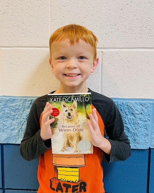 Image_student holding a book receiving recognition for academics or behavior.