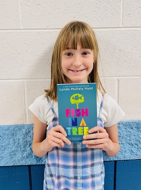 Image_student holding a book receiving recognition for academics or behavior.