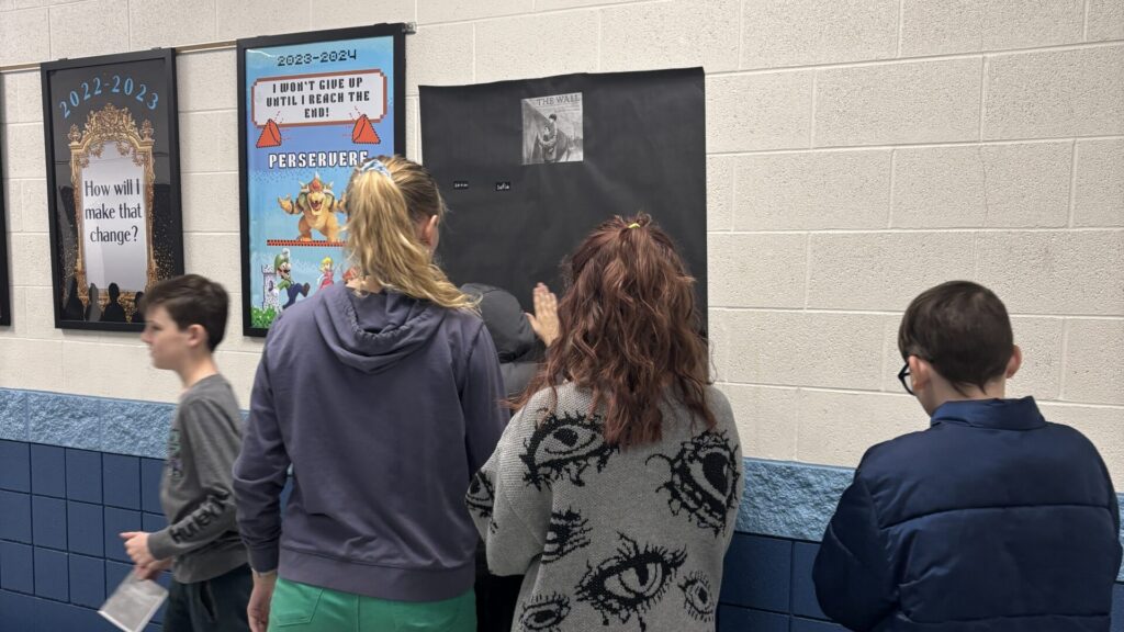 students involved in a reading challenge place their names on the wall next to the books they read.